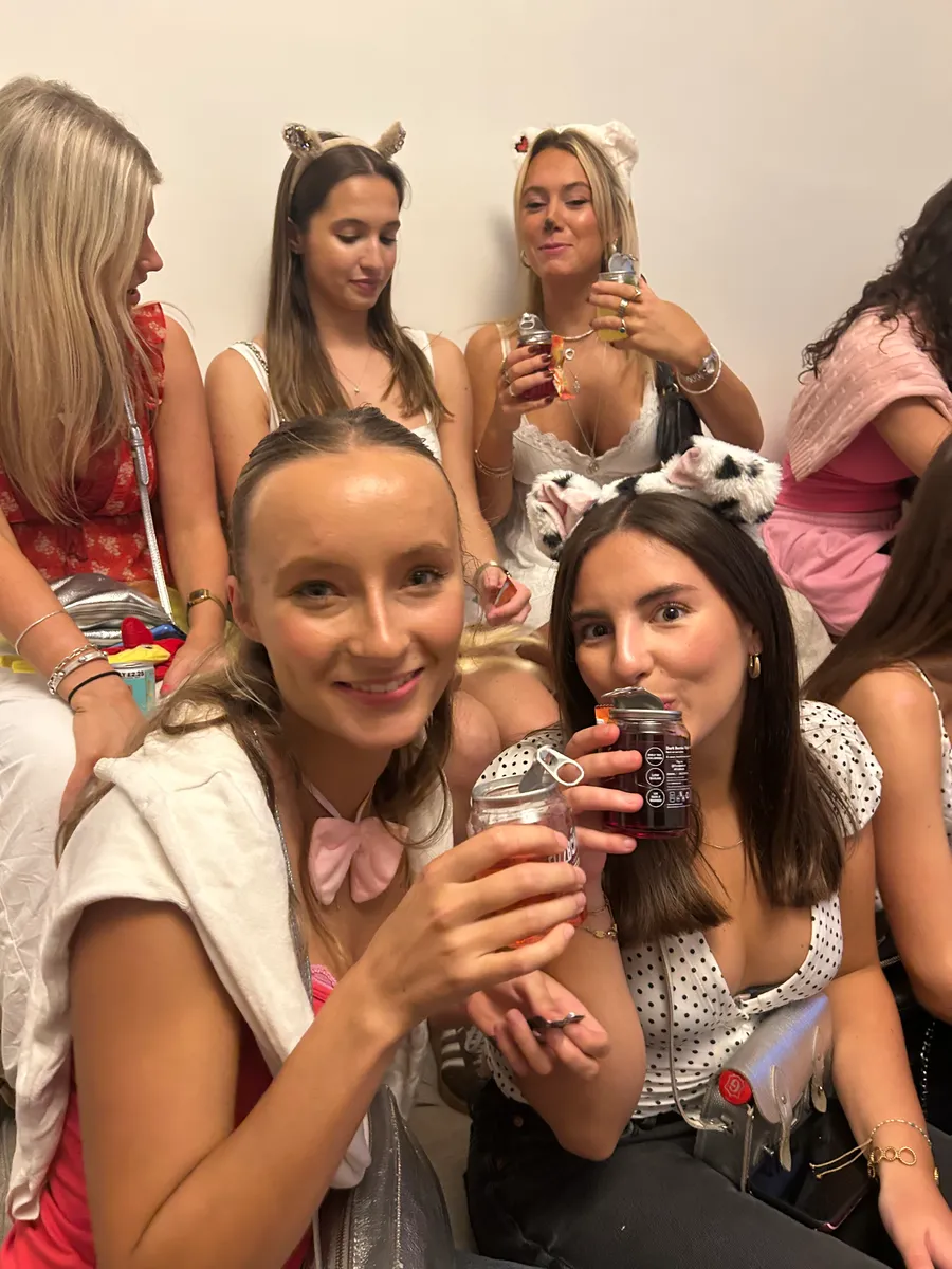 A friend smiling with her FizzBomb can while the friend beside her takes a sip of hers