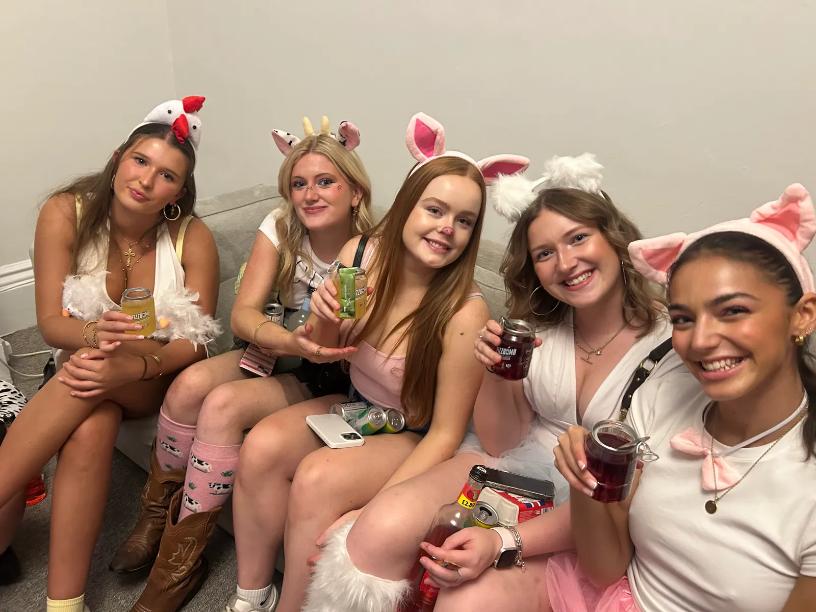Five friends in farmyard fancy dress on a sofa, holding up their FizzBomb cans