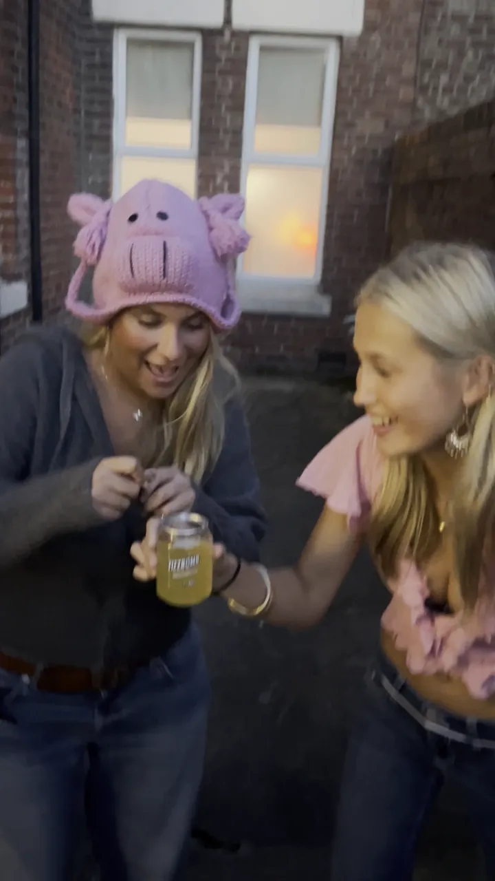 Two friends outside at dusk, one tearing a Party Powder sachet open over the other's FizzBomb can
